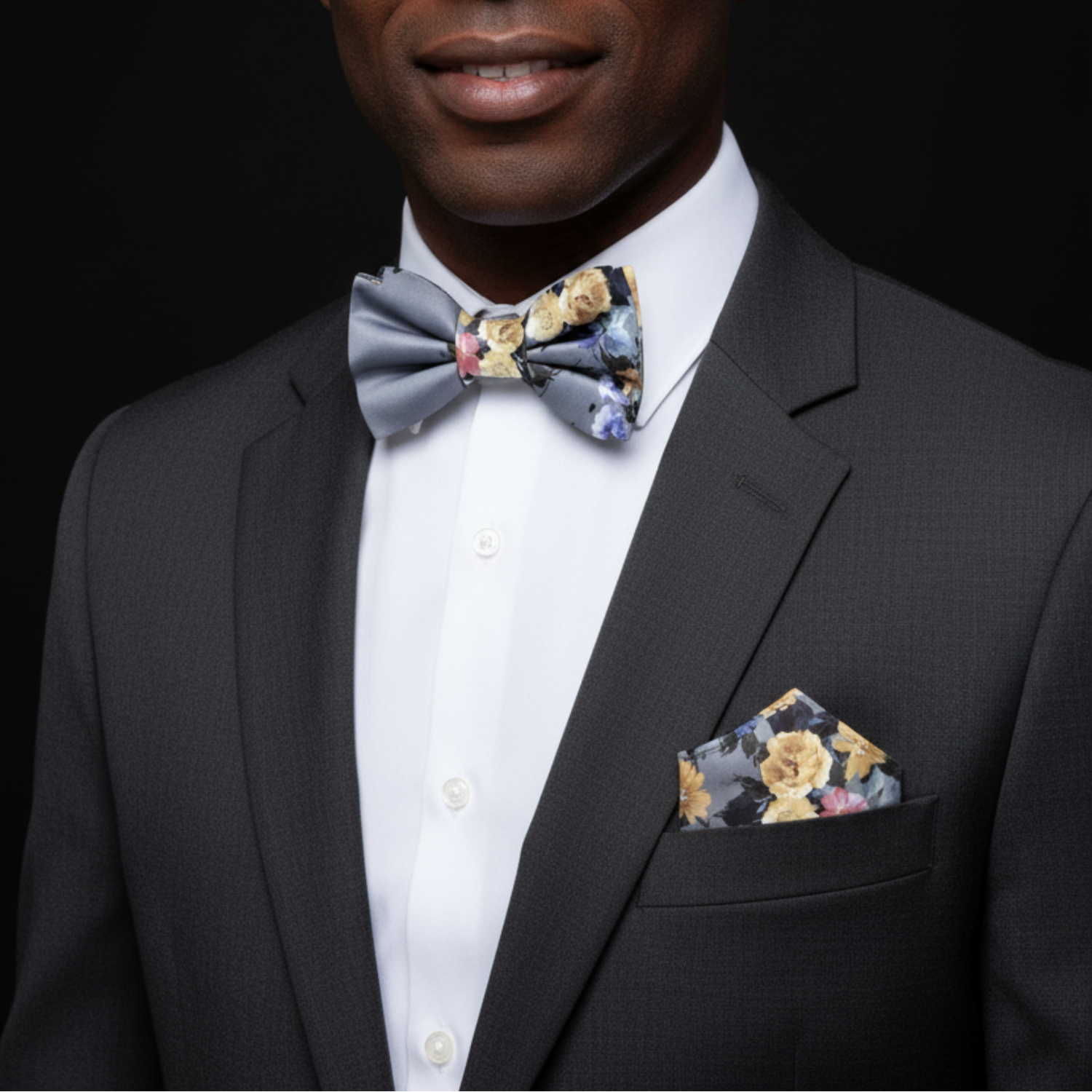 Man wearing a black suit with a floral bow tie and pocket square against a dark background