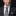 Man wearing a dark suit with a patterned tie and pocket square against a black background