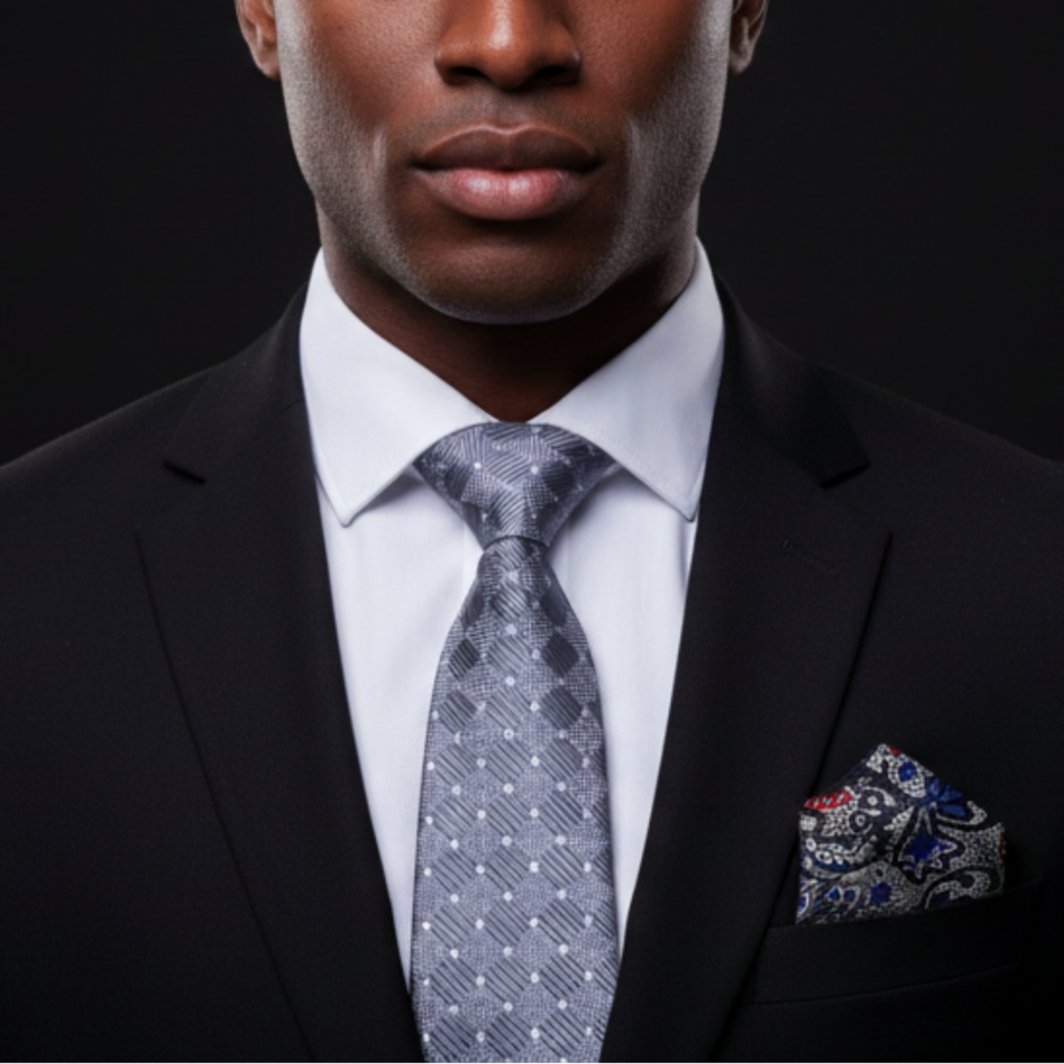Man wearing a black suit with a patterned tie and pocket square on a dark background
