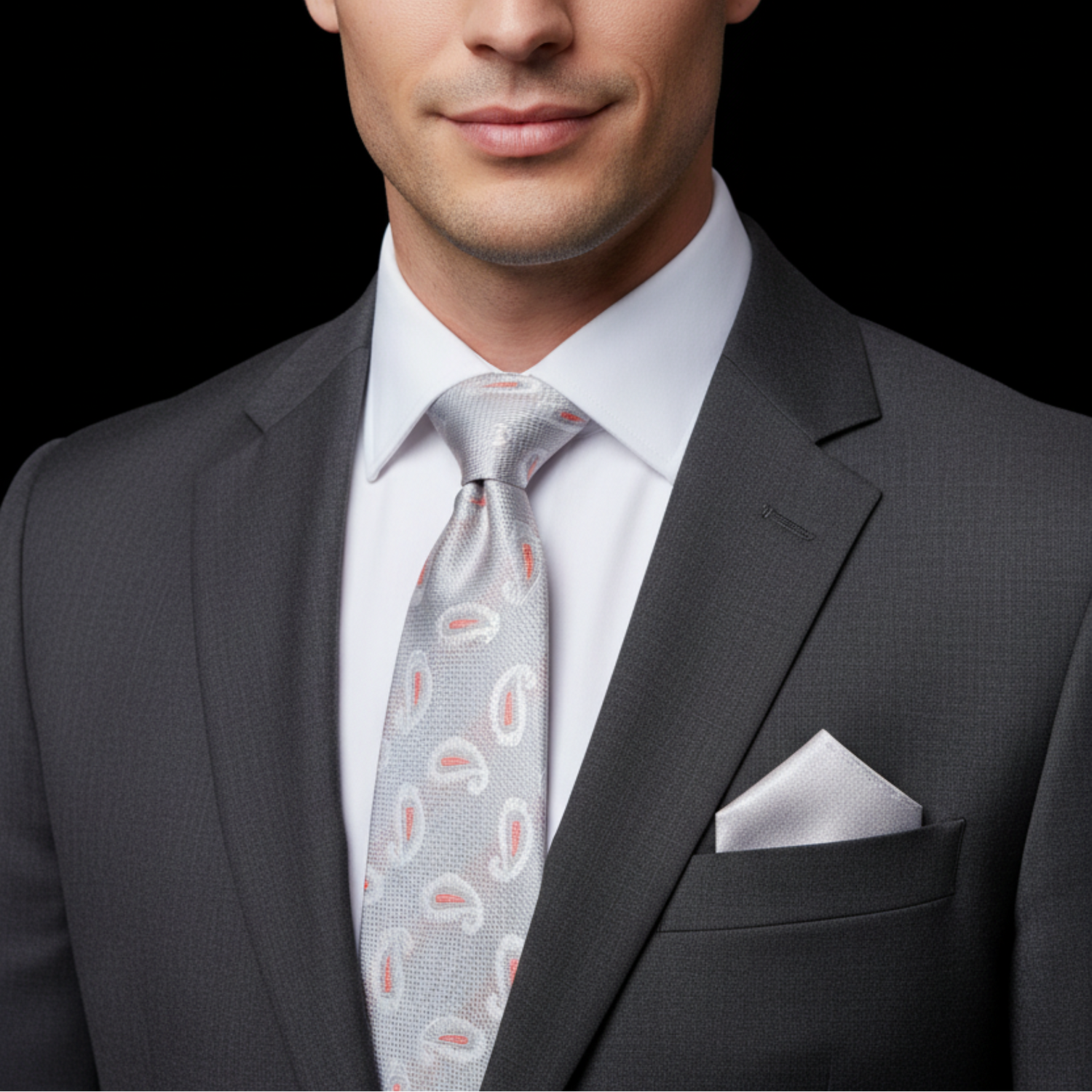 Man wearing a gray suit with a patterned tie and pocket square on a black background