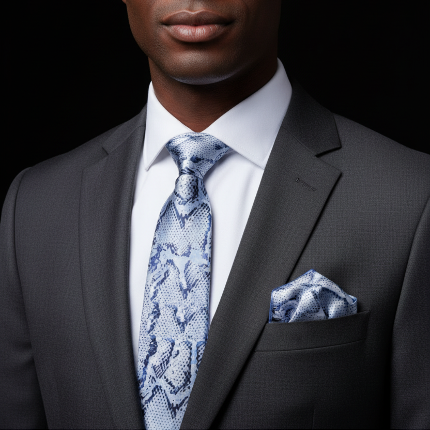 Man wearing a gray suit with a blue patterned tie and pocket square on a black background