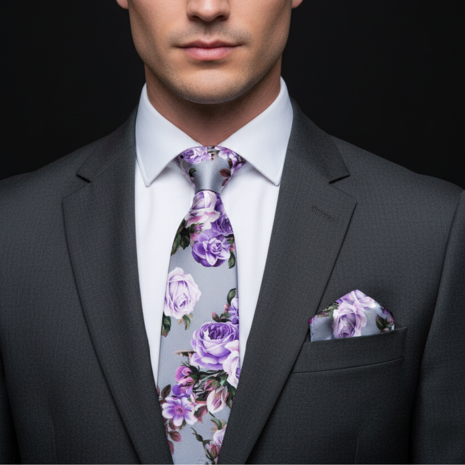 Man wearing a gray suit with a floral tie and pocket square on a black background