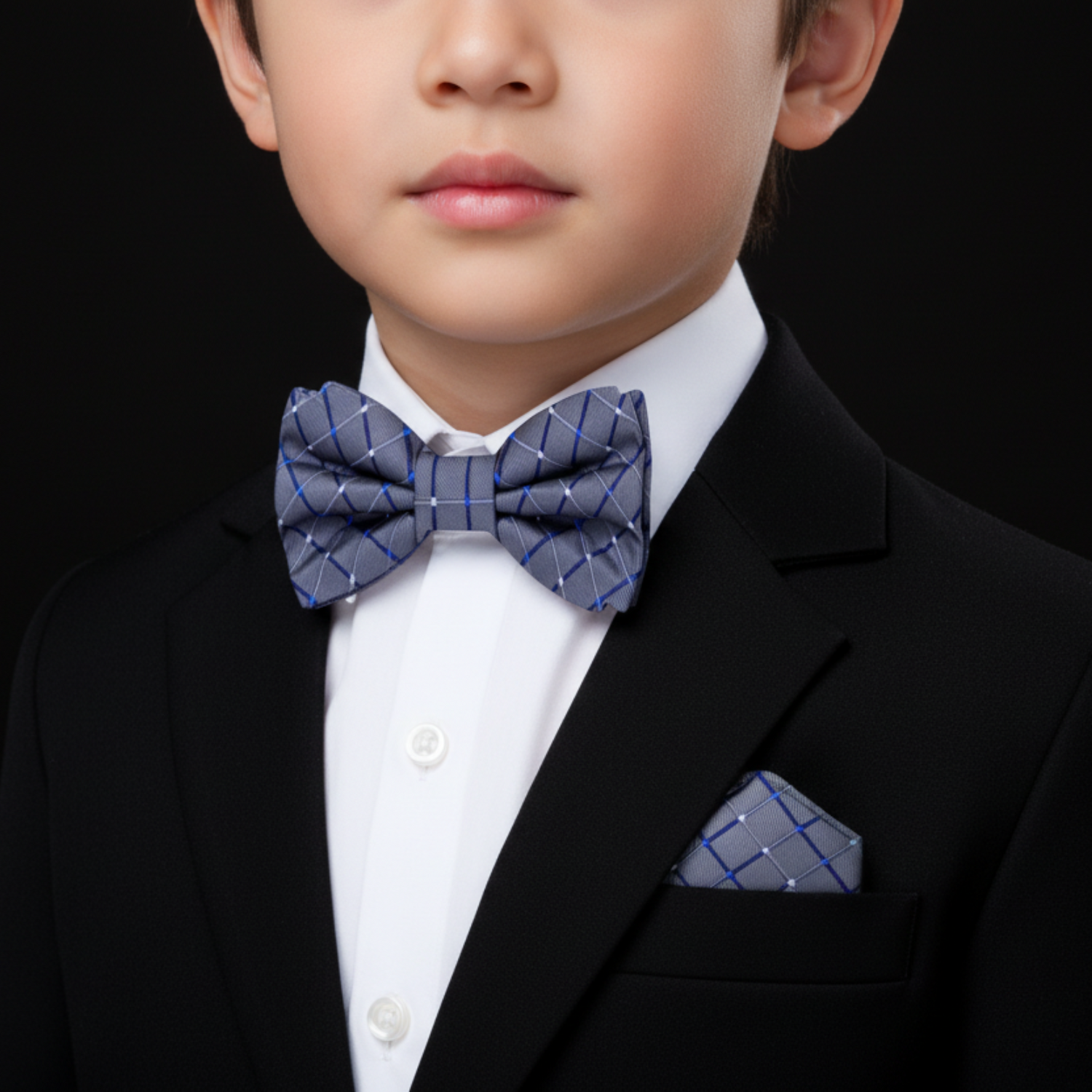 Child wearing a black suit with a white shirt and blue checkered bow tie and pocket square on a black background
