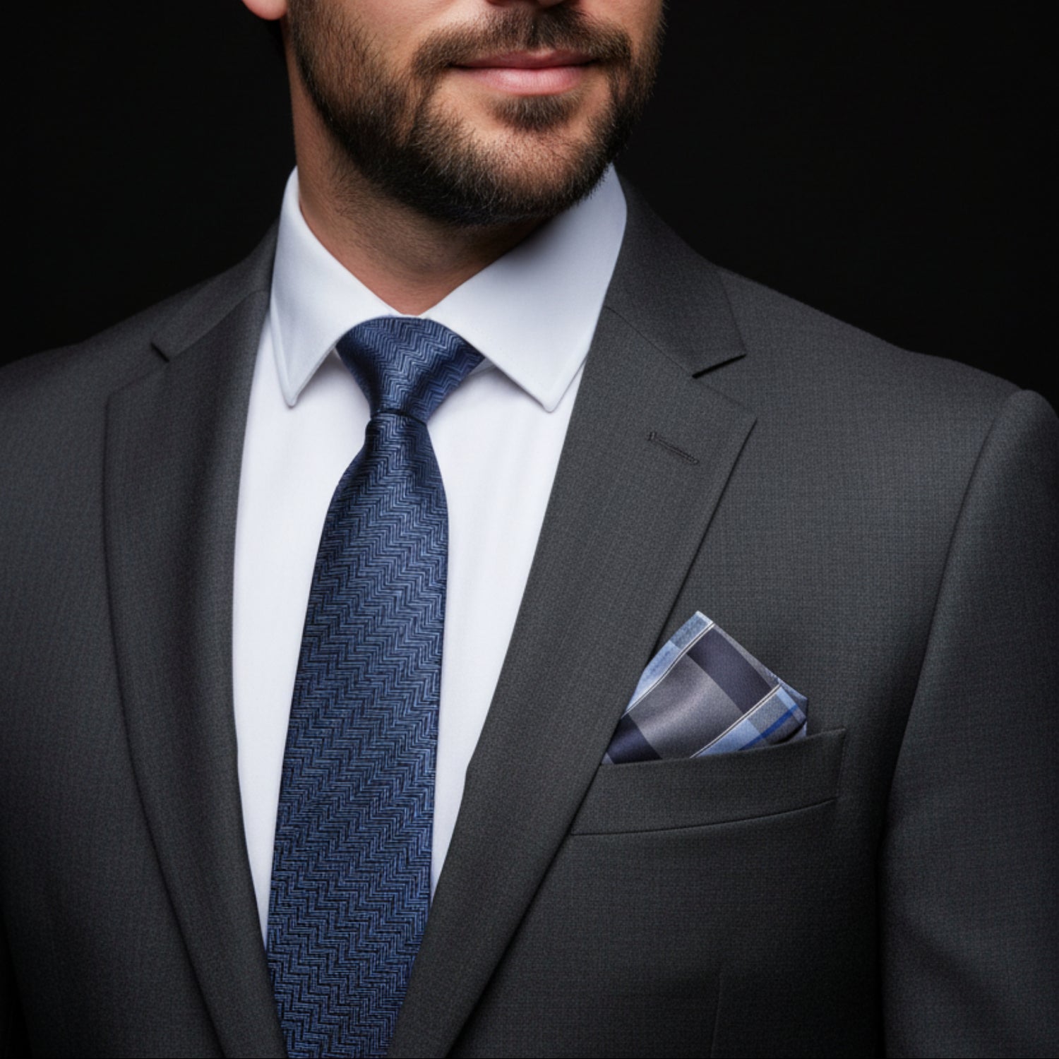 Man wearing a gray suit with a blue tie and pocket square on a black background