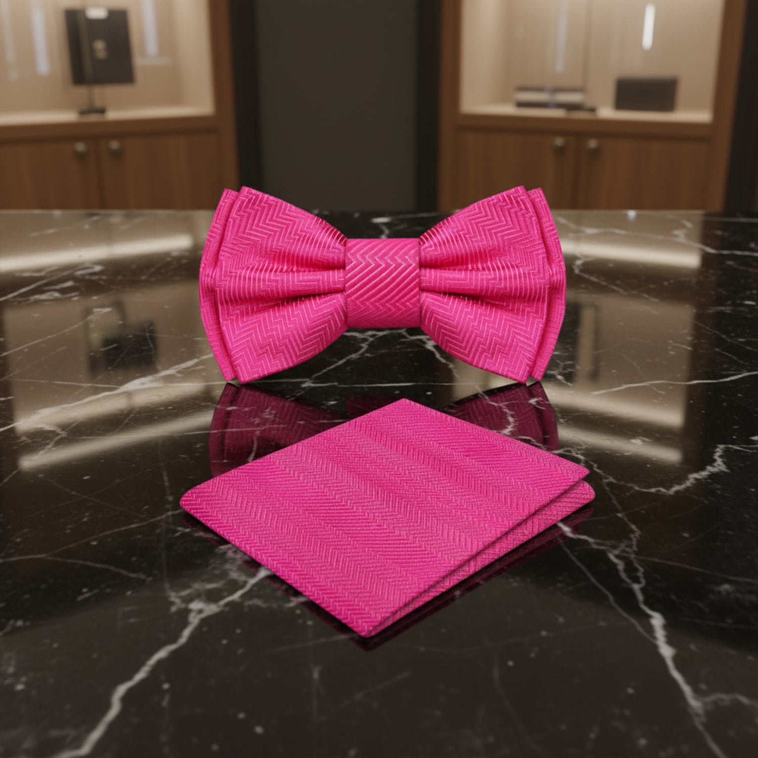 Pink bow tie and matching pocket square on a dark marble surface with gold accents.