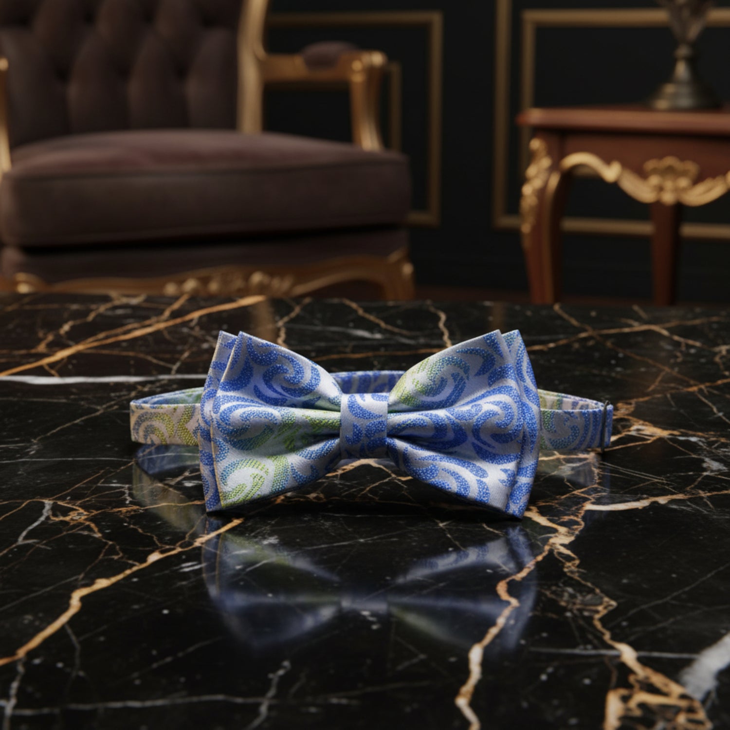 A pre-tied bow tie with a matching neck strap, featuring a blue and green paisley pattern on a white background, shown against a plain white backdrop.