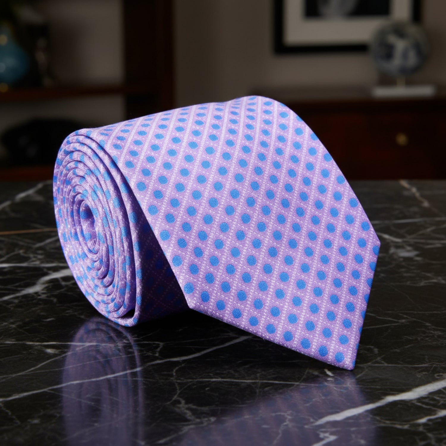 Rolled purple tie with blue polka dots on a marble surface