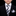 Child wearing a black suit with a white shirt and patterned tie on a black background