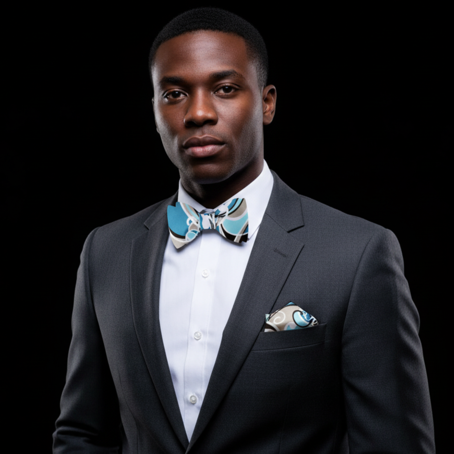 Man wearing a black suit with a white shirt and patterned bow tie on a black background