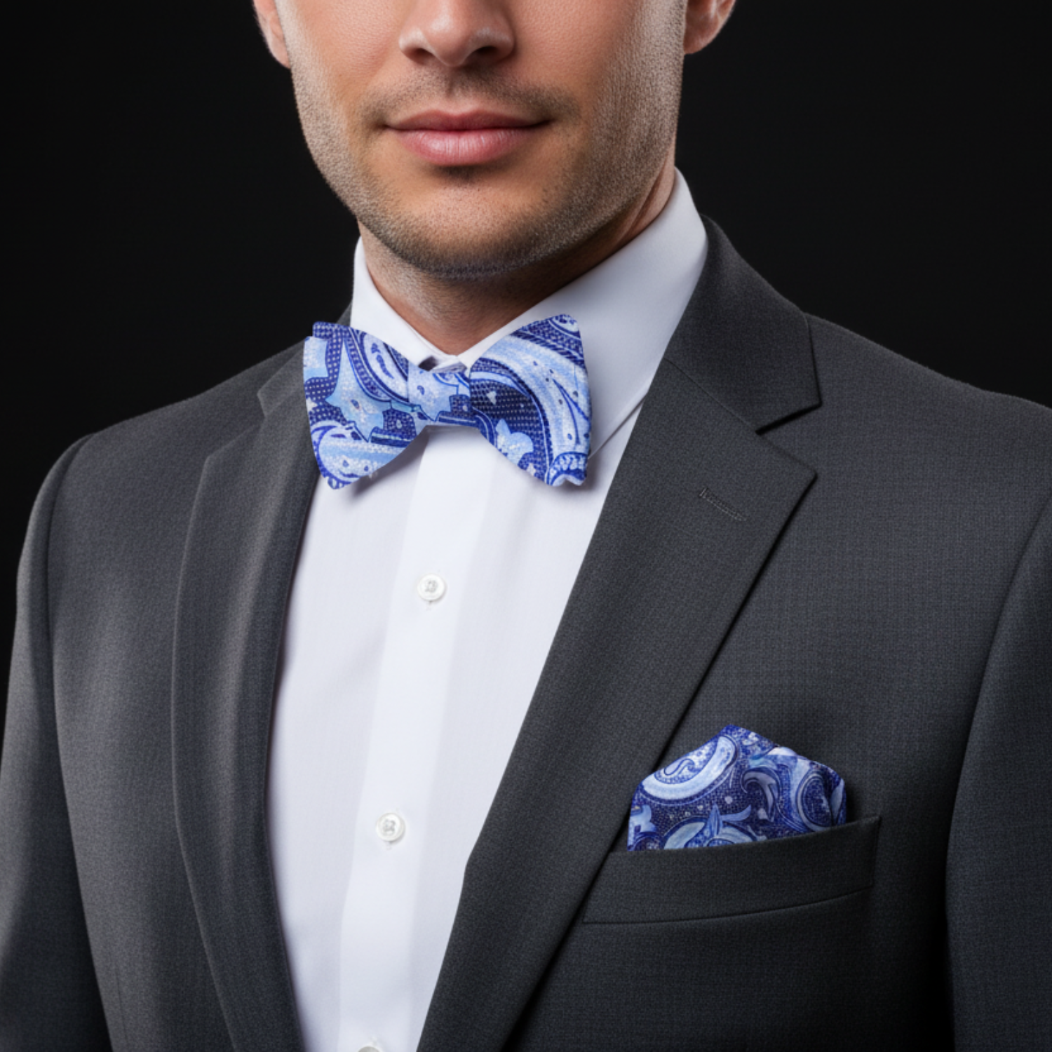 Man wearing a gray suit with a white shirt, blue bow tie, and matching pocket square on a black background.