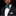 Man wearing a black suit with a white shirt and teal bow tie on a black background