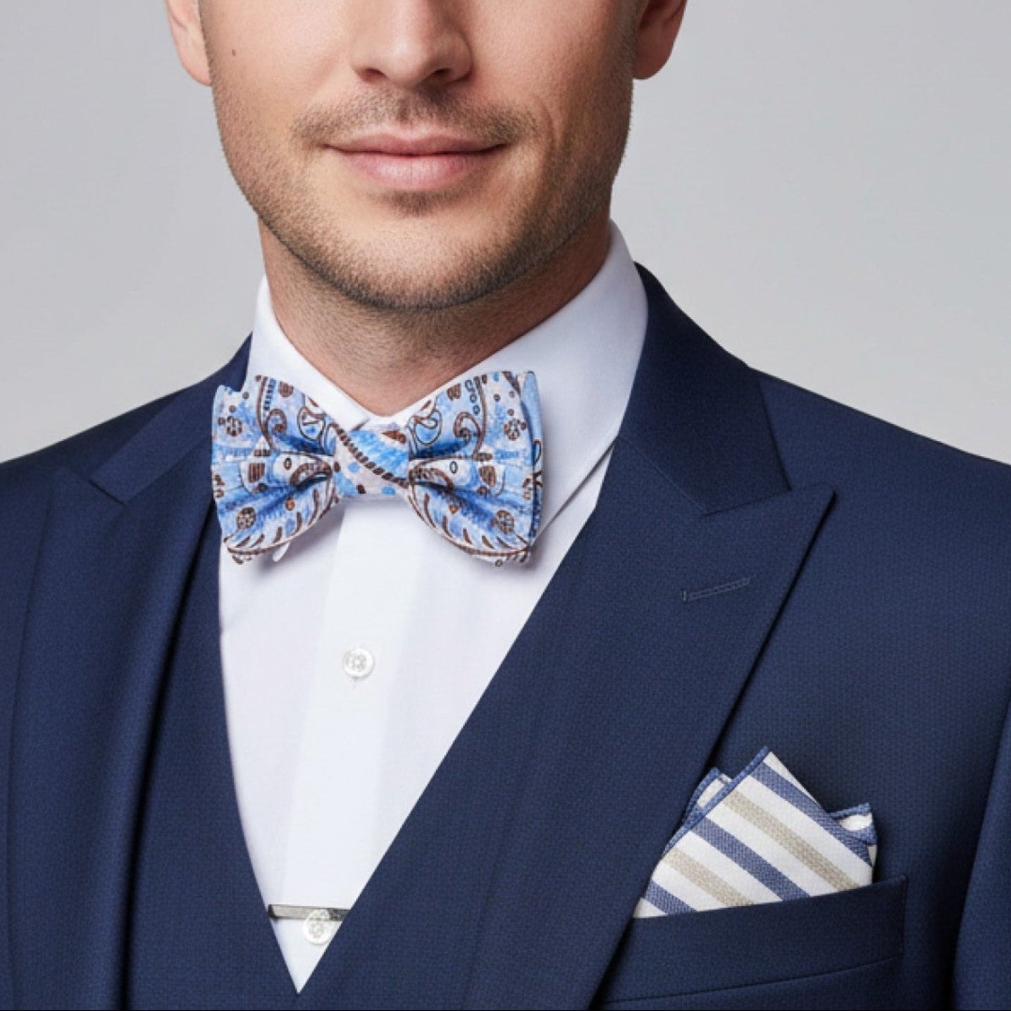 Man wearing a navy suit with a patterned bow tie and pocket square on a gray background