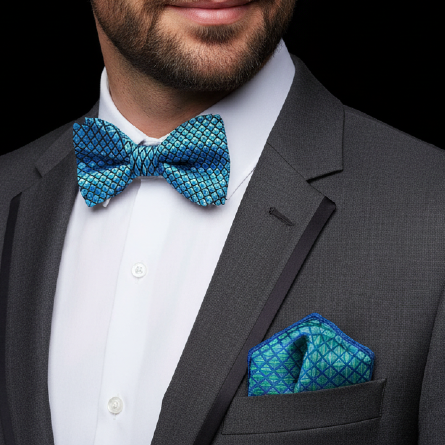 Man wearing a gray suit with a blue patterned bow tie and pocket square on a black background