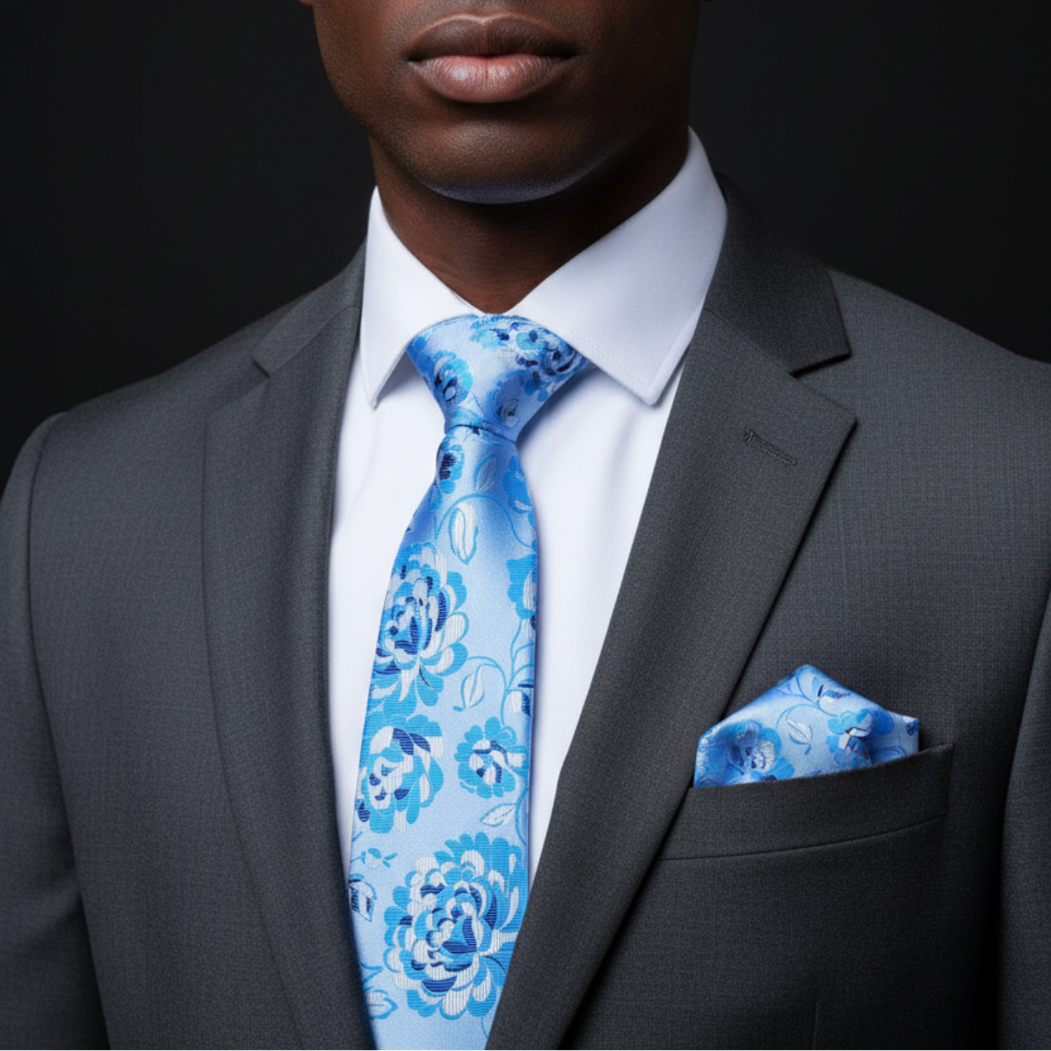 Man wearing a gray suit with a blue floral tie and pocket square on a black background
