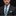 Man wearing a black suit with a blue and green checkered tie and pocket square on a dark background