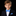 A young boy with light brown hair is wearing a blue patterned bow tie and matching pocket square with a navy suit jacket and white dress shirt, set against a solid black background.