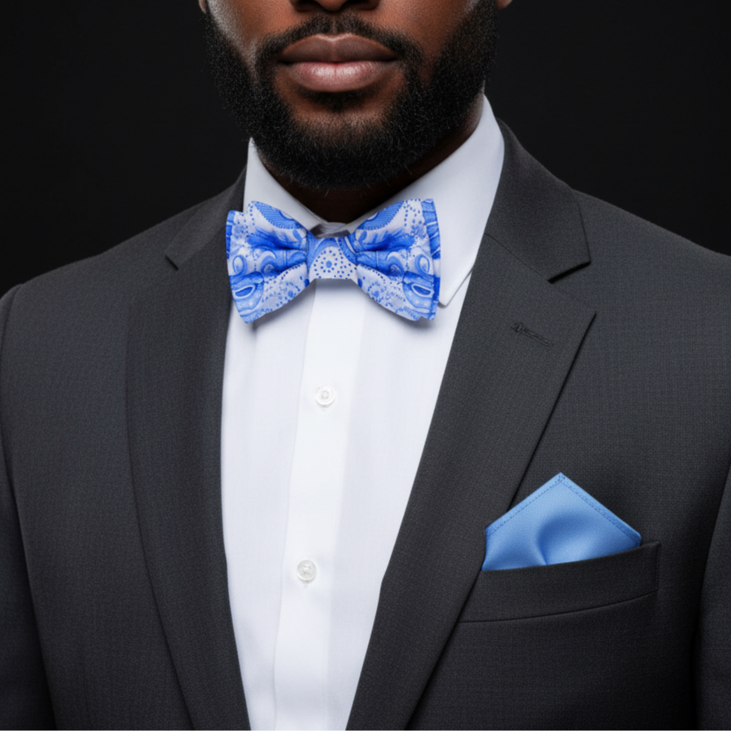 Man wearing a black suit with a white shirt and blue bow tie and pocket square against a black background