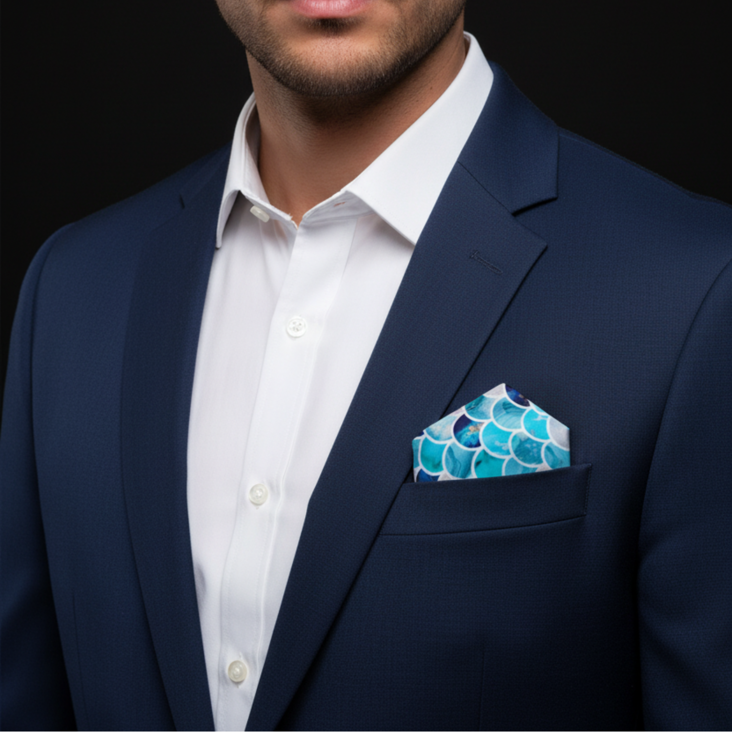 Man wearing a navy suit with a white shirt and blue patterned pocket square on a black background