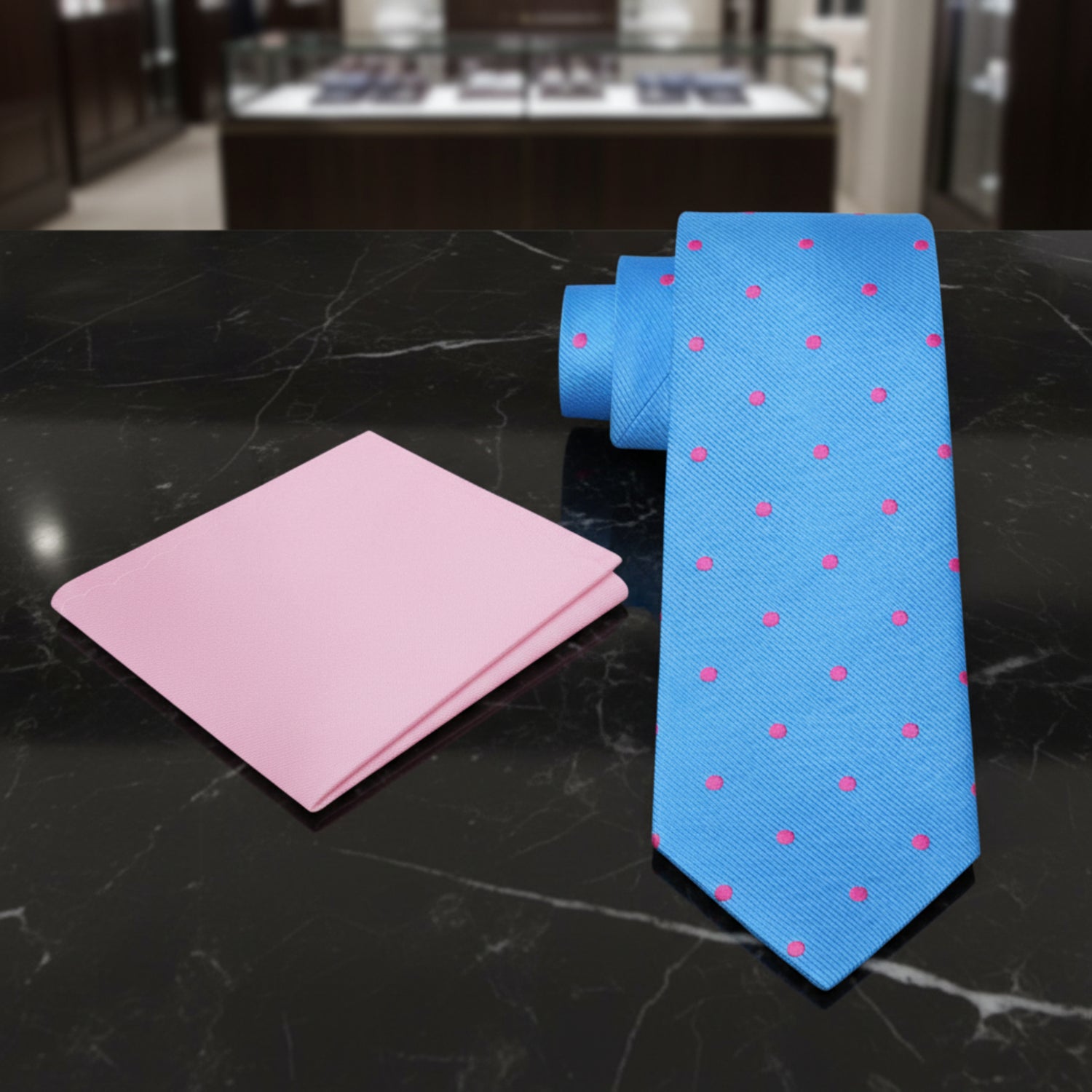 Blue tie with pink polka dots and pink pocket square on a black marble background 