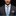Man wearing a gray suit with a blue tie and striped pocket square on a black background