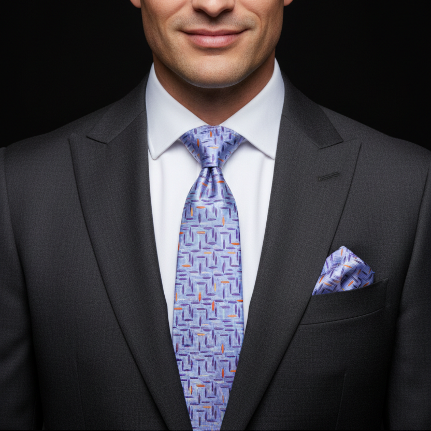 Man wearing a dark suit with a patterned blue tie and pocket square on a black background