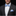 Man wearing a black suit with a blue bow tie and pocket square on a black background