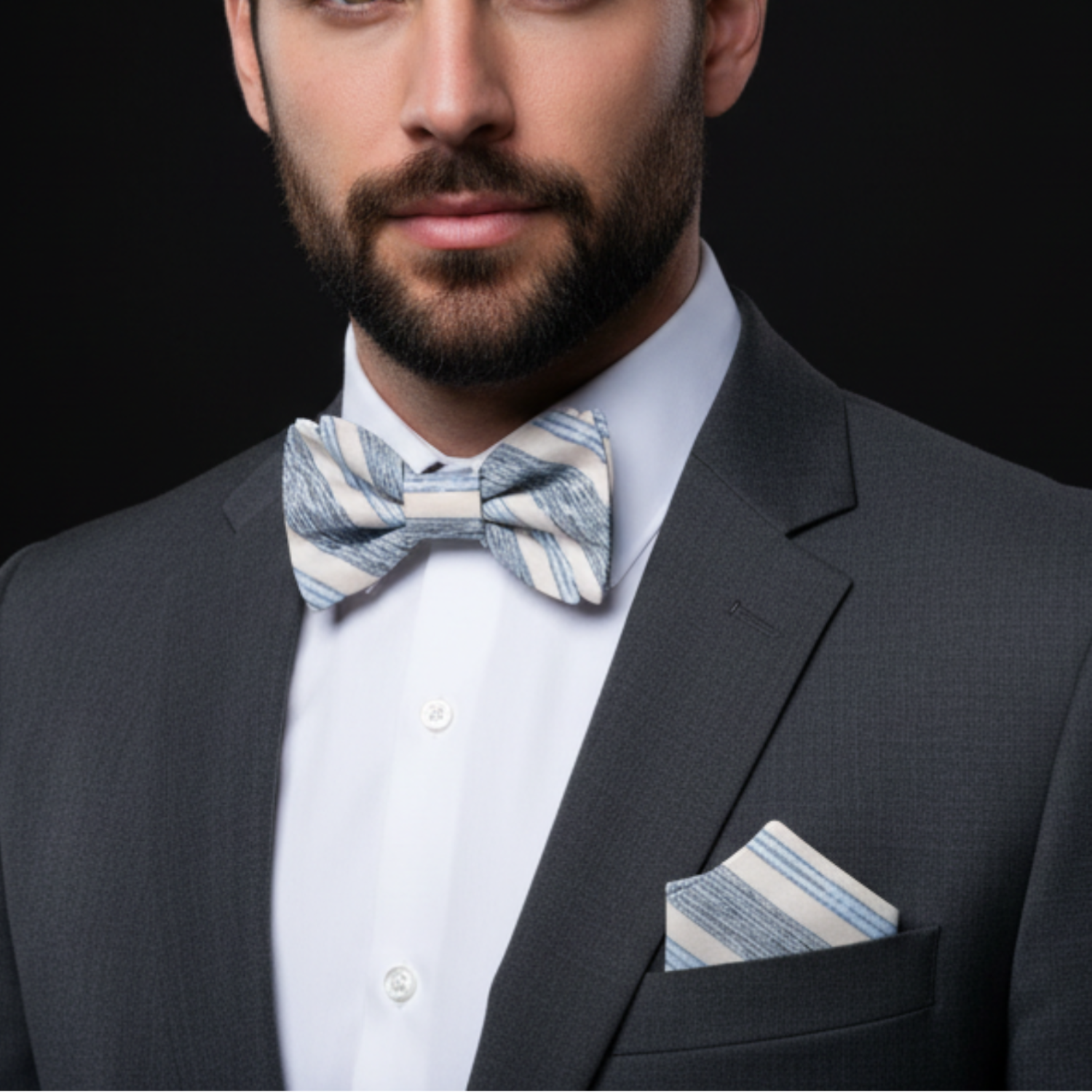 Man wearing a gray suit with a striped bow tie and pocket square against a black background