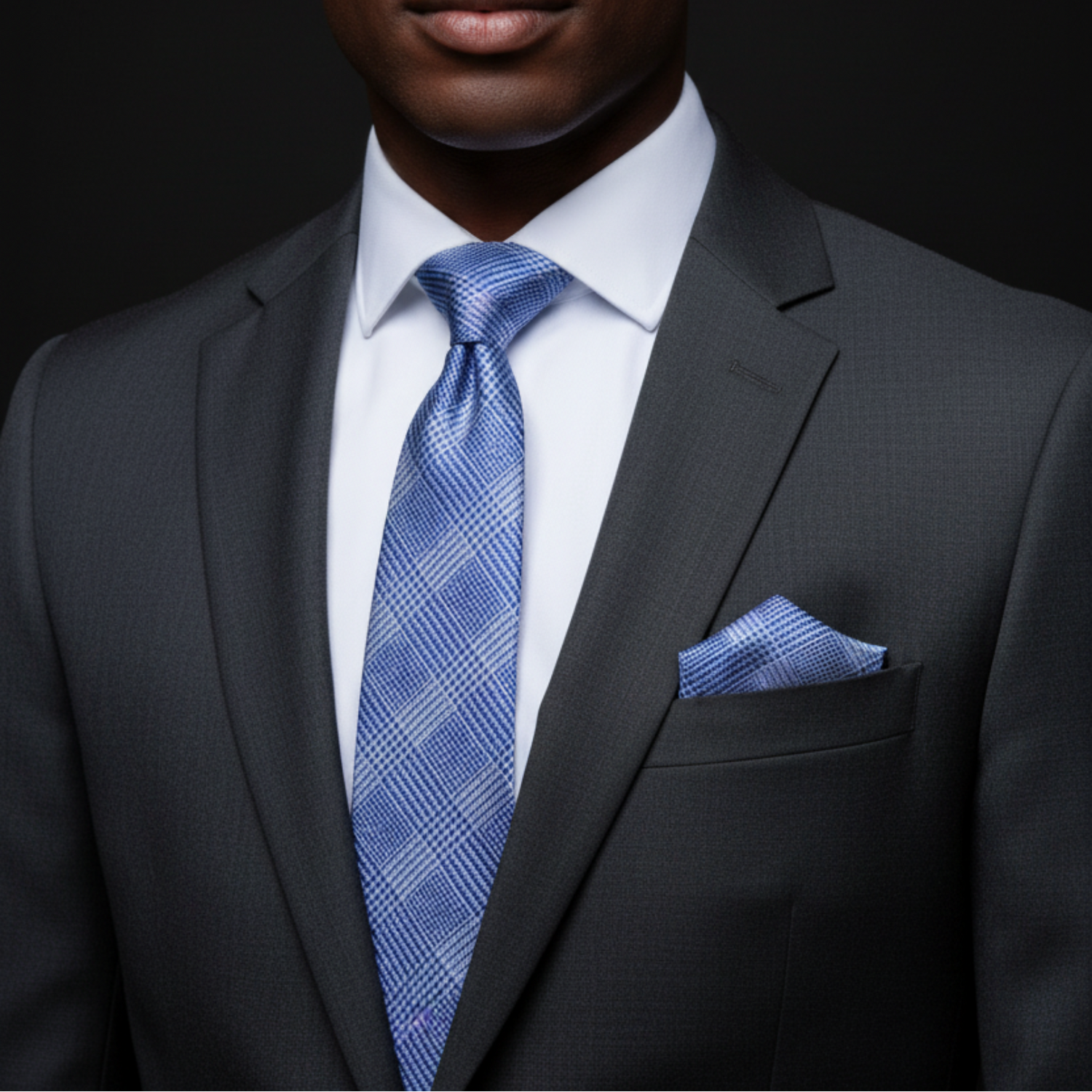 Man wearing a dark gray suit with a blue patterned tie and pocket square on a black background