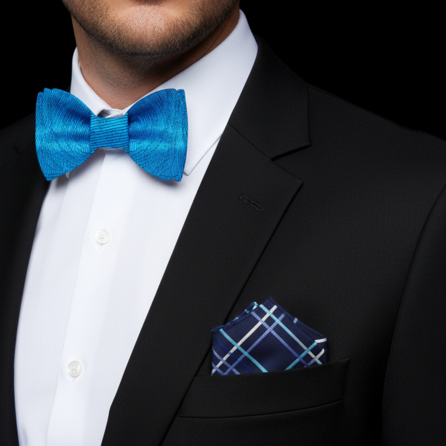Man wearing a black suit with a blue bow tie and accenting pocket square on a black background