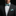 Man wearing a black suit with a white shirt, teal bow tie, and matching pocket square against a black background.