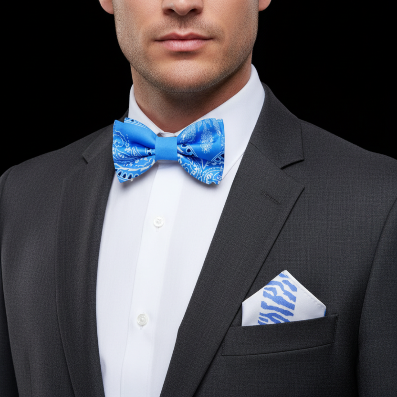 Man wearing a black suit with a white shirt, blue bow tie, and matching pocket square on a black background.