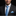 Man wearing a black suit with a white shirt and blue tie and pocket square against a black background