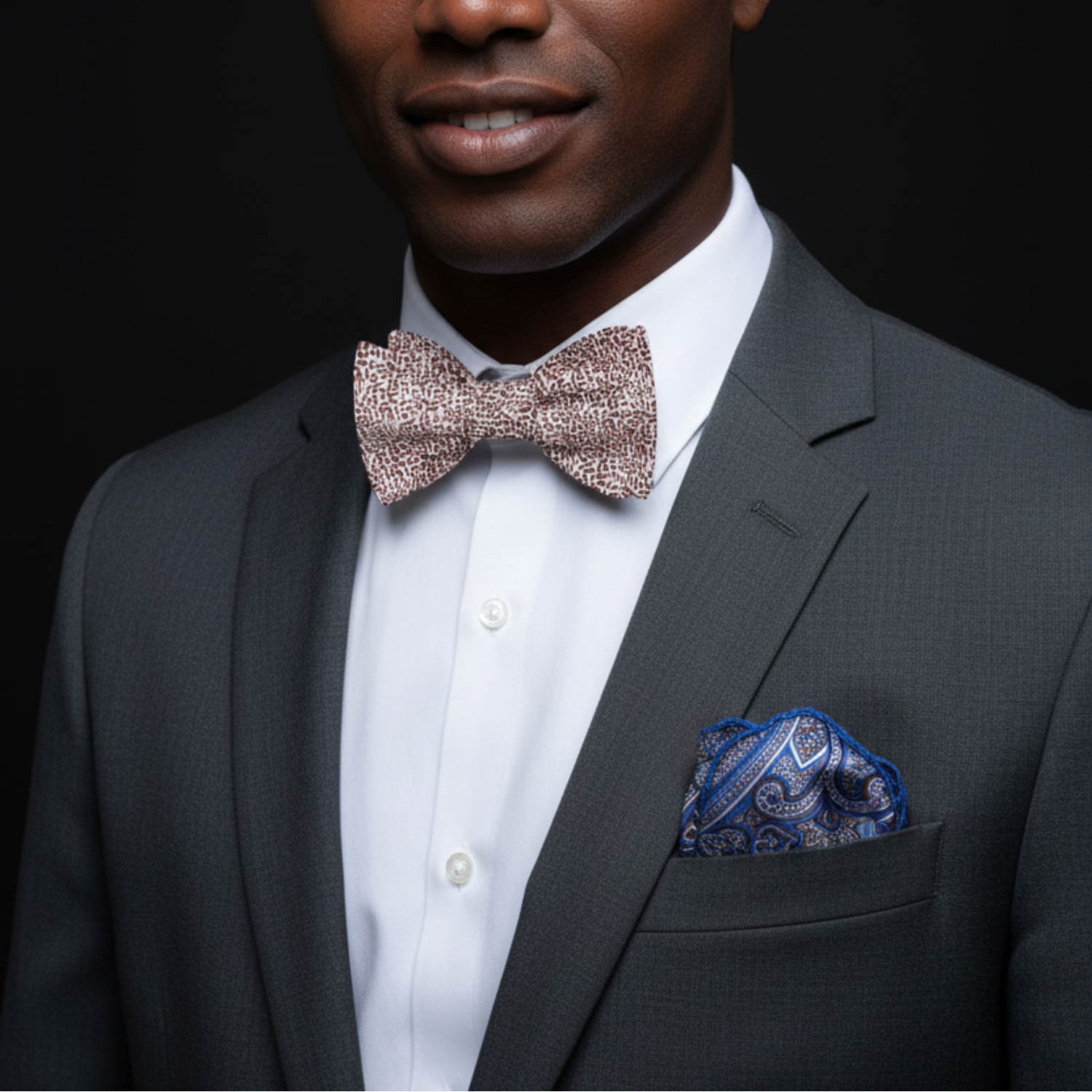Man wearing a gray suit with a patterned bow tie and pocket square on a black background