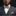 Man wearing a gray suit with a gold bow tie and pocket square against a black background