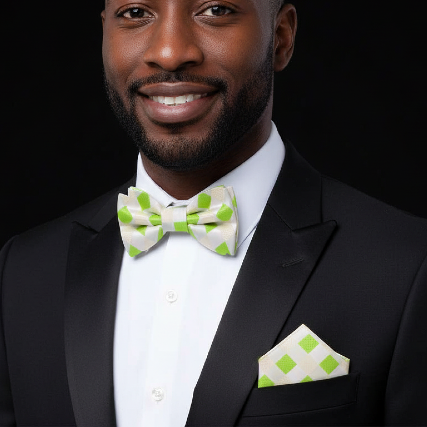 Man wearing a black tuxedo with a green and white bow tie and pocket square against a dark background