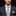 Man wearing a gray suit with a patterned tie and pocket square against a black background