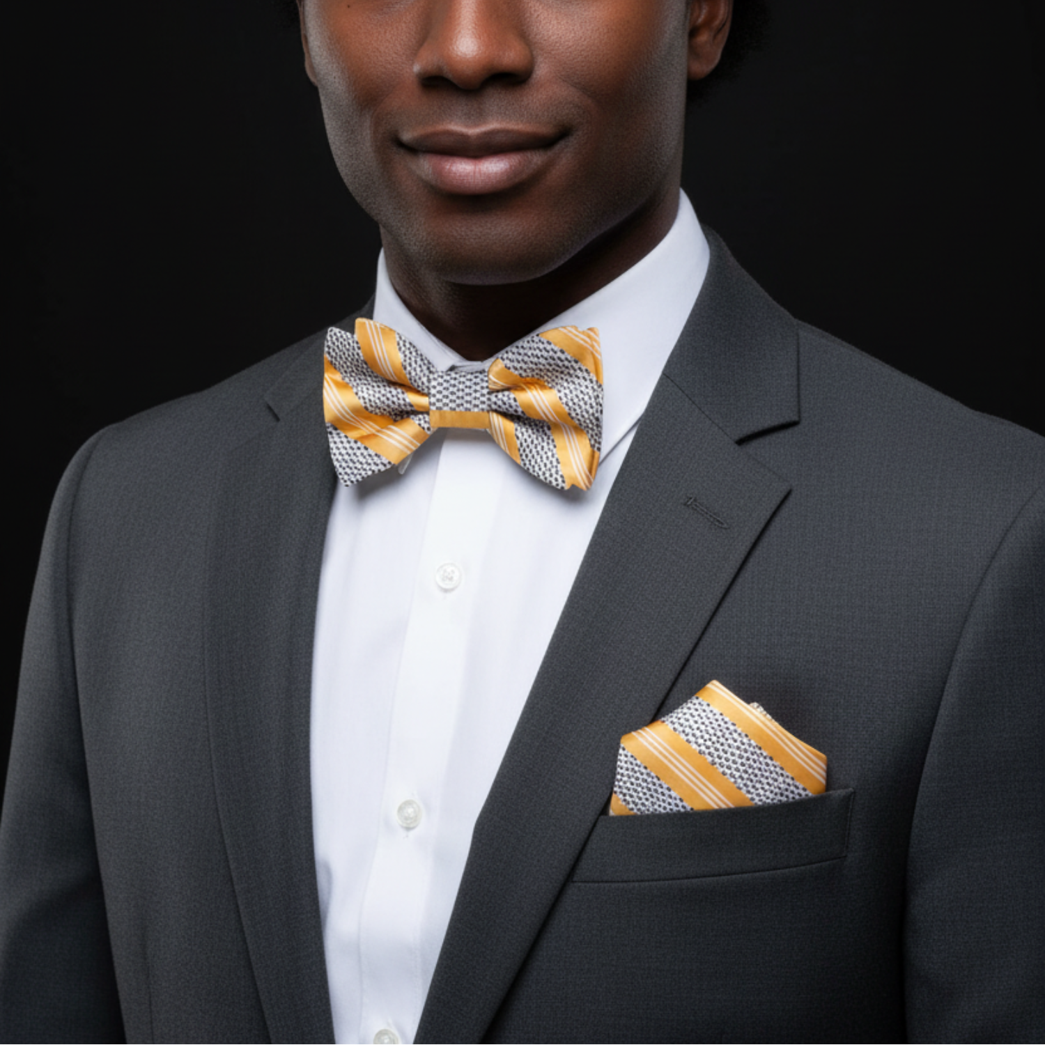 Man wearing a gray suit with a yellow and gray patterned bow tie and pocket square against a black background