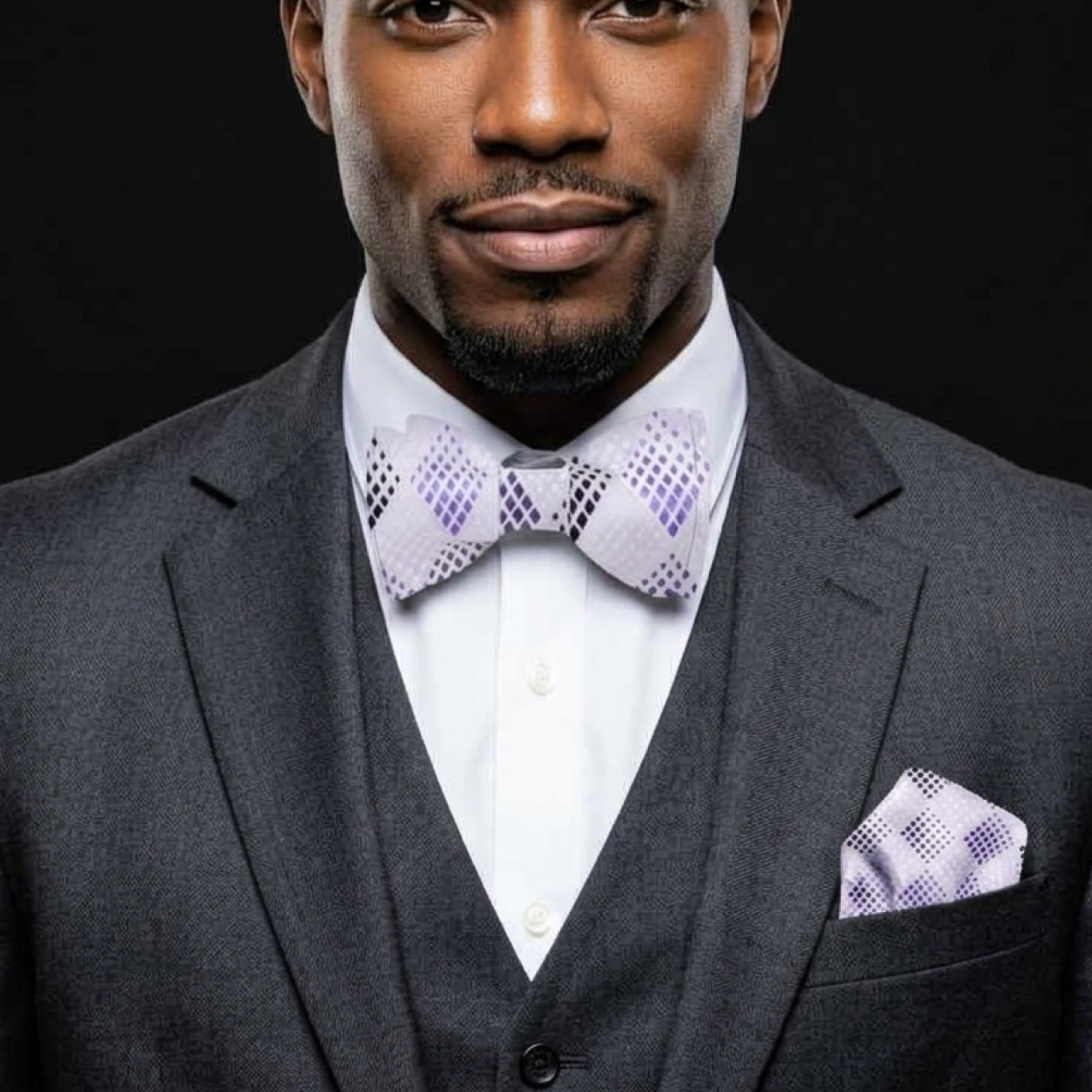 Man wearing a gray suit with a purple bow tie and pocket square against a black background