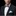 Man wearing a black suit with a patterned bow tie and light blue pocket square on a black background