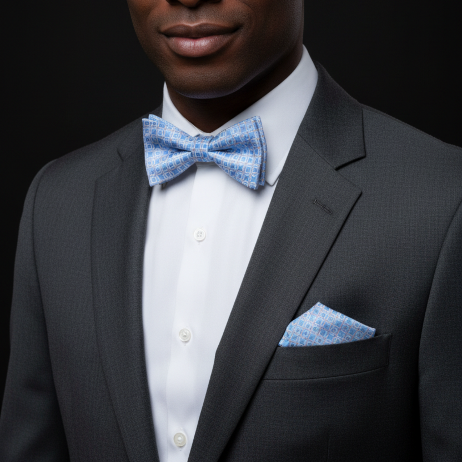 Man wearing a black suit with a white shirt and blue bow tie against a black background