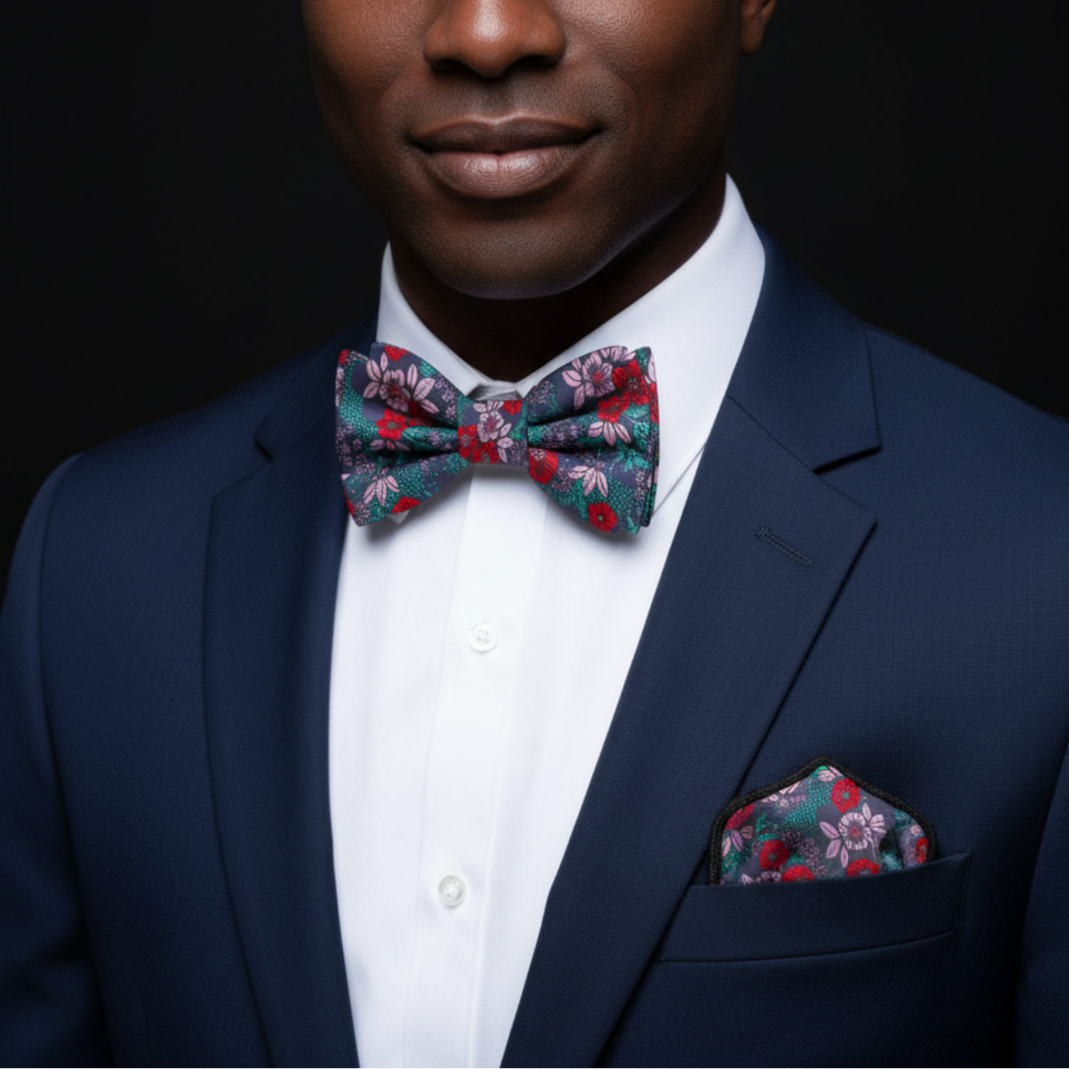 Man wearing a navy suit with a floral bow tie and pocket square on a black background