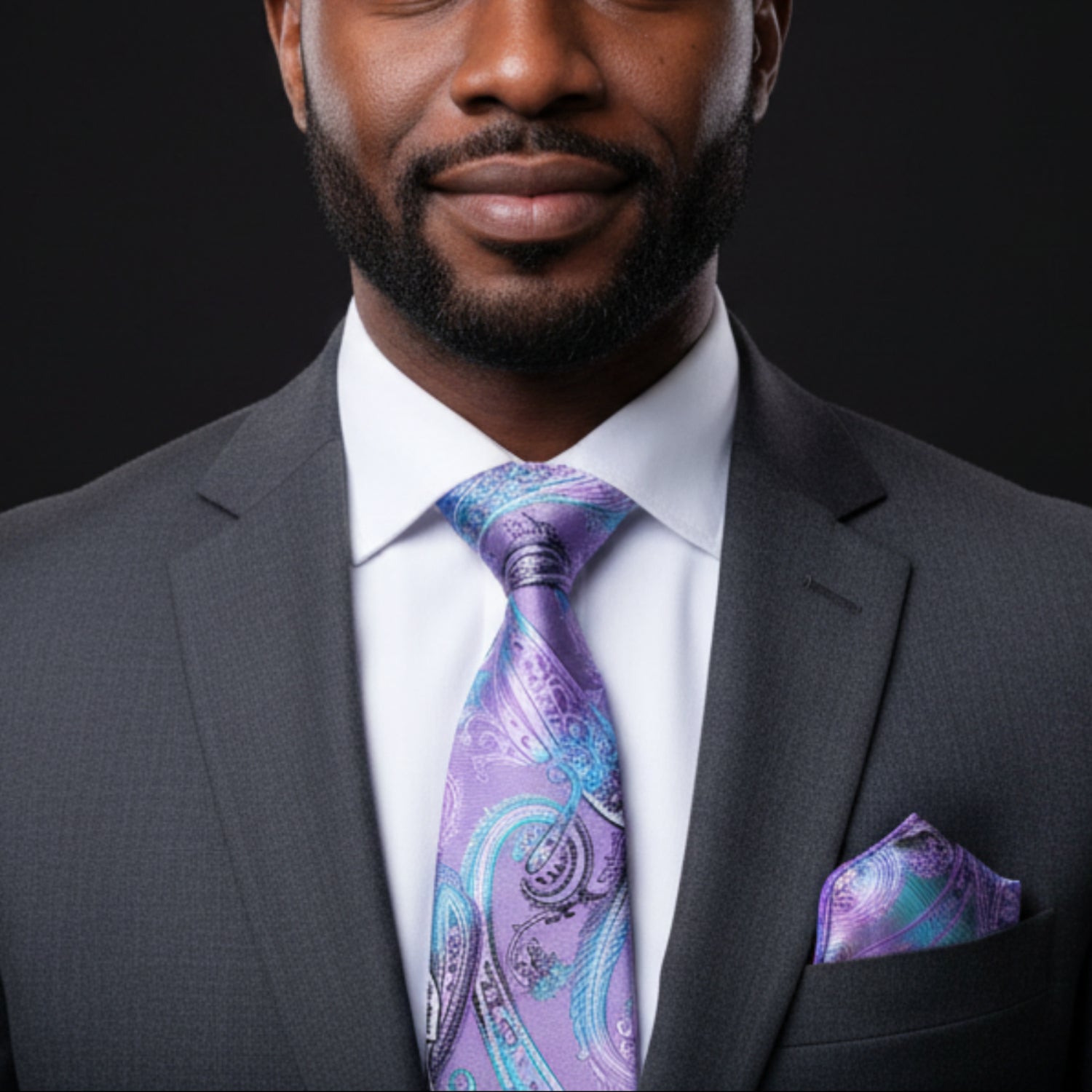 Man wearing a gray suit with a purple paisley tie and pocket square on a black background