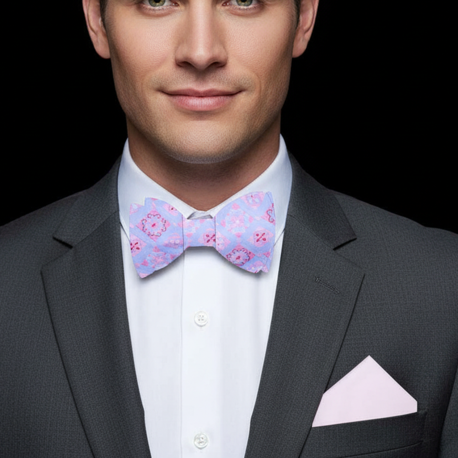 Man wearing a gray suit with a pink bow tie and pocket square on a black background