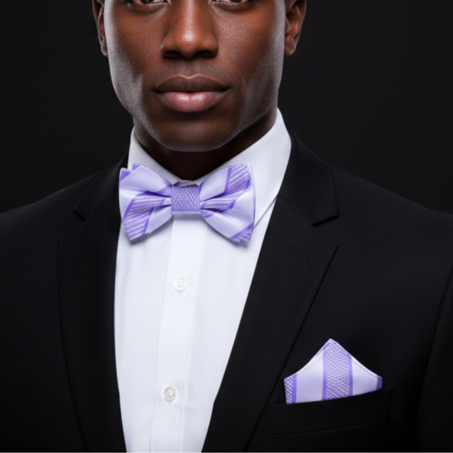 Man wearing a black suit with a purple bow tie and pocket square on a dark background