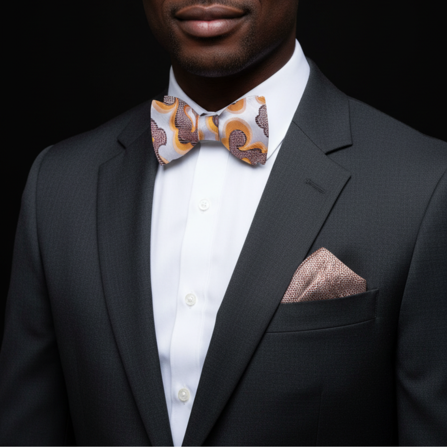 Man wearing a dark suit with a patterned bow tie and pocket square against a black background