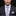 Man wearing a dark suit with a white shirt and purple striped tie against a black background