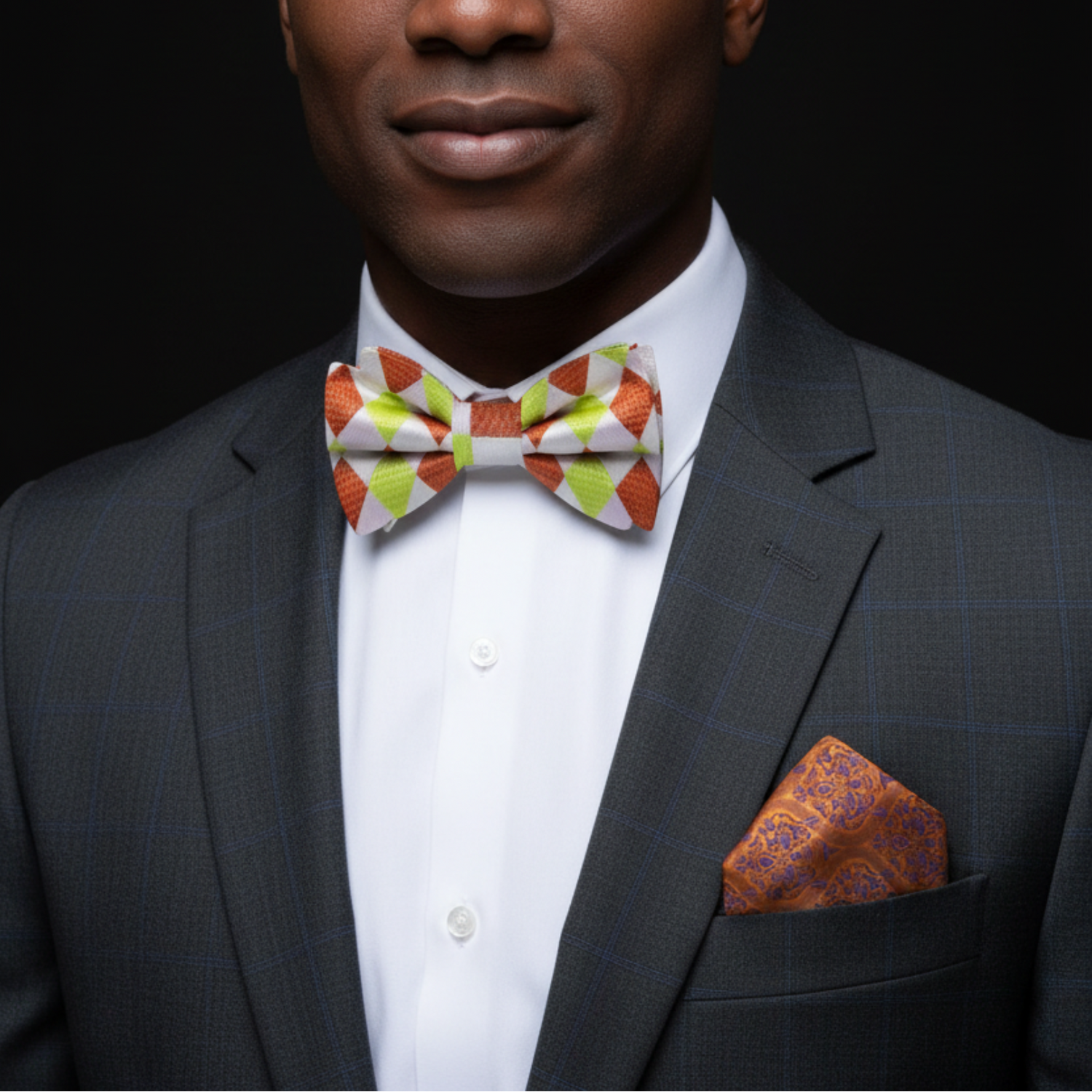 Man wearing a gray suit with a colorful bow tie and pocket square against a black background