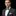 Man wearing a dark suit with a green bow tie and pocket square on a black background