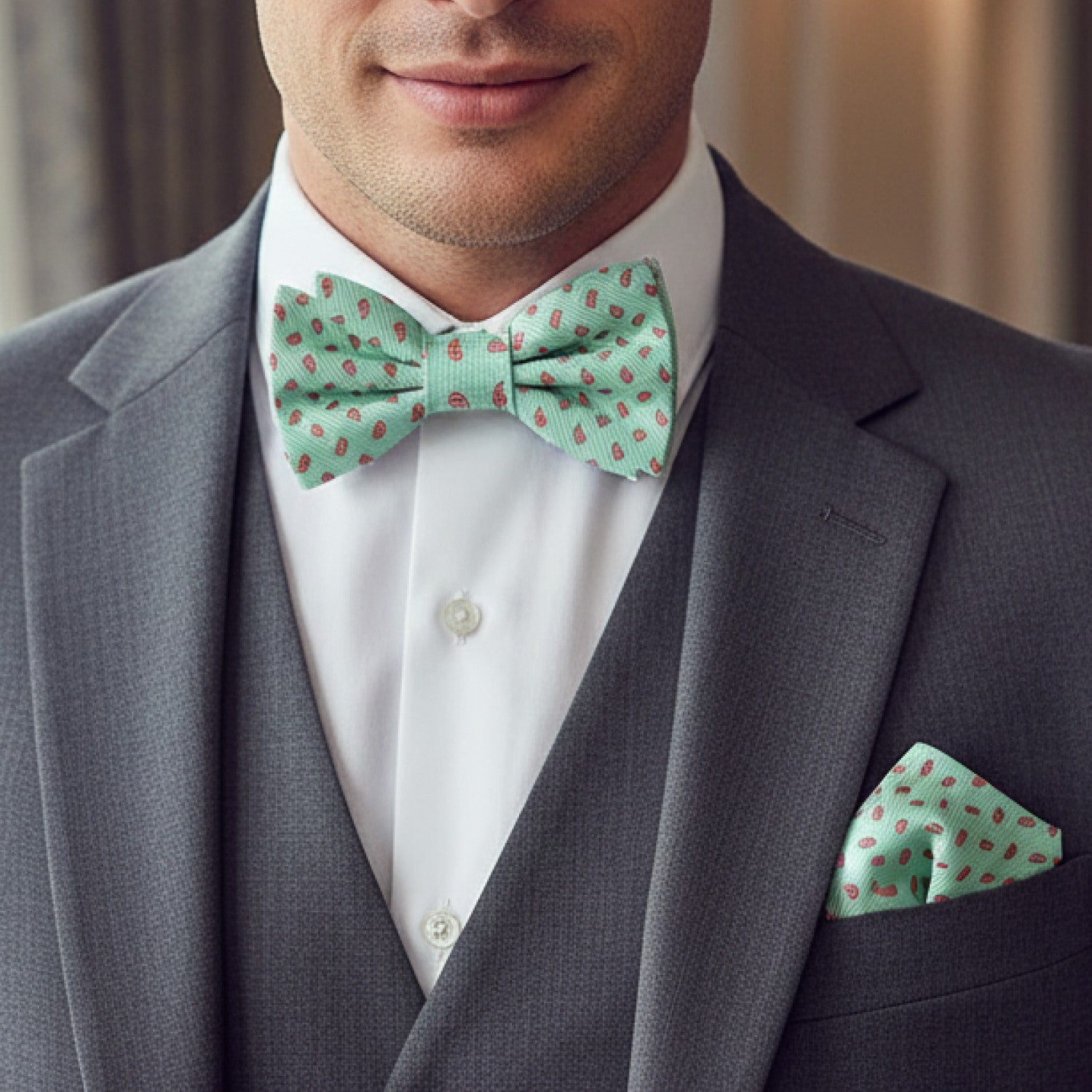 Man wearing a gray suit with a white shirt, green bow tie, and matching pocket square.