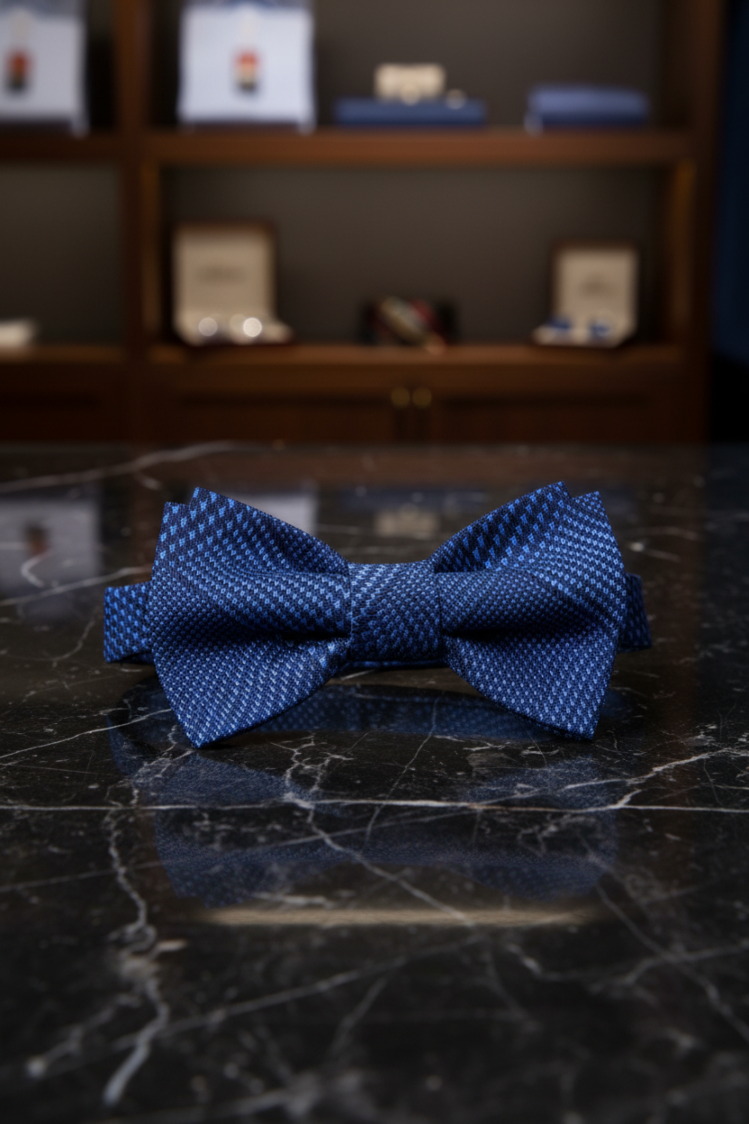 Blue bow tie on a dark marble surface with blurred shelves in the background